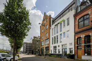 Straatbeeld van de De Ruijterkade in Amsterdam met diverse kantoorgebouwen en historische gevels.